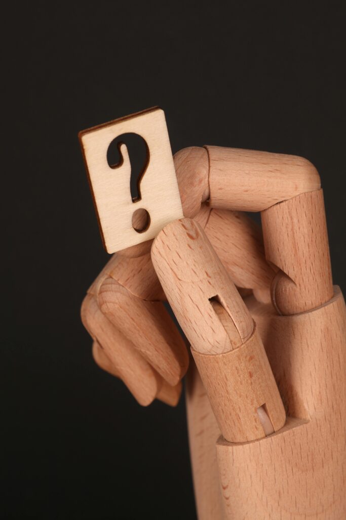 Close-up of a wooden hand holding a question mark on a black background.