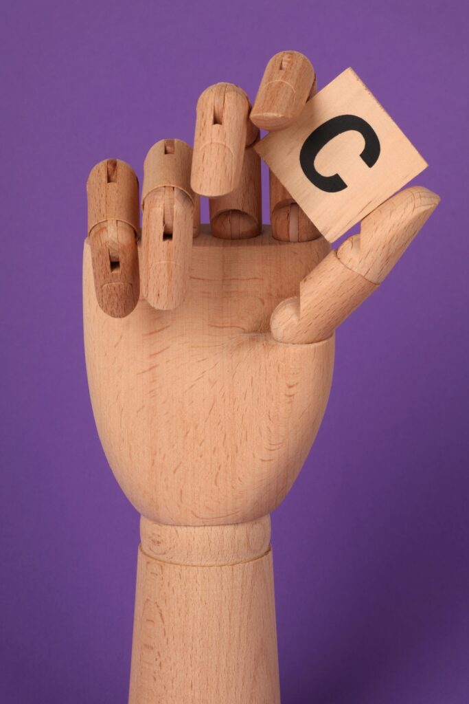Wooden mannequin hand holds a letter block against a vibrant purple backdrop.