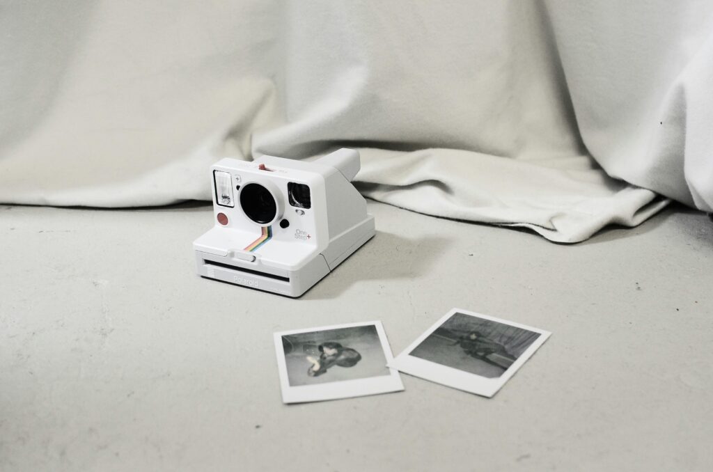 Modern instant photo camera and instant photos placed on floor near light curtain